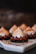 Delicate pastries with a chocolate base, topped with swirls of chocolate ganache and a lightly toasted meringue. The pastries are artfully arranged on a white platter with small nut pieces scattered around.