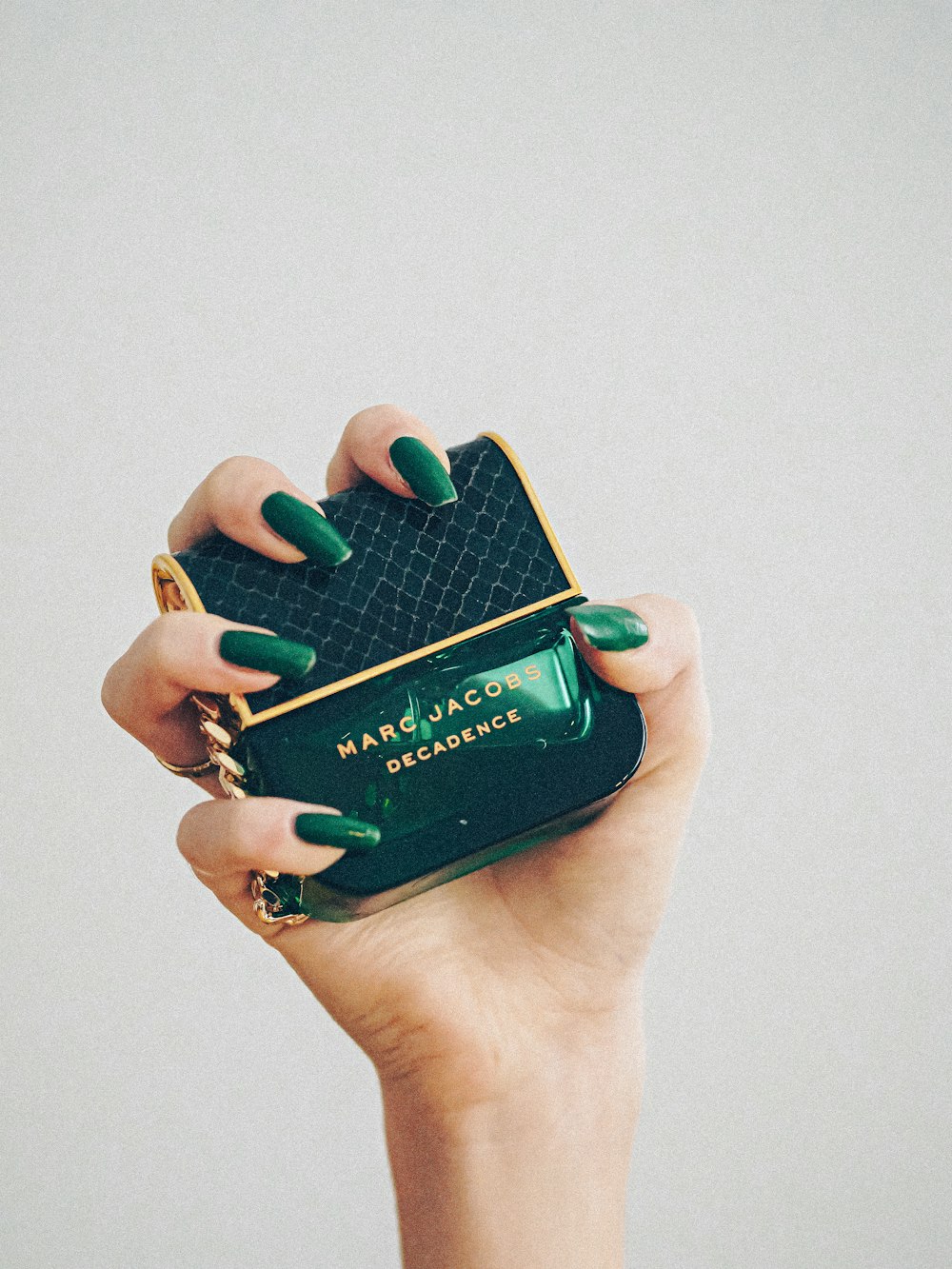 a hand holding a green purse with a green manicure