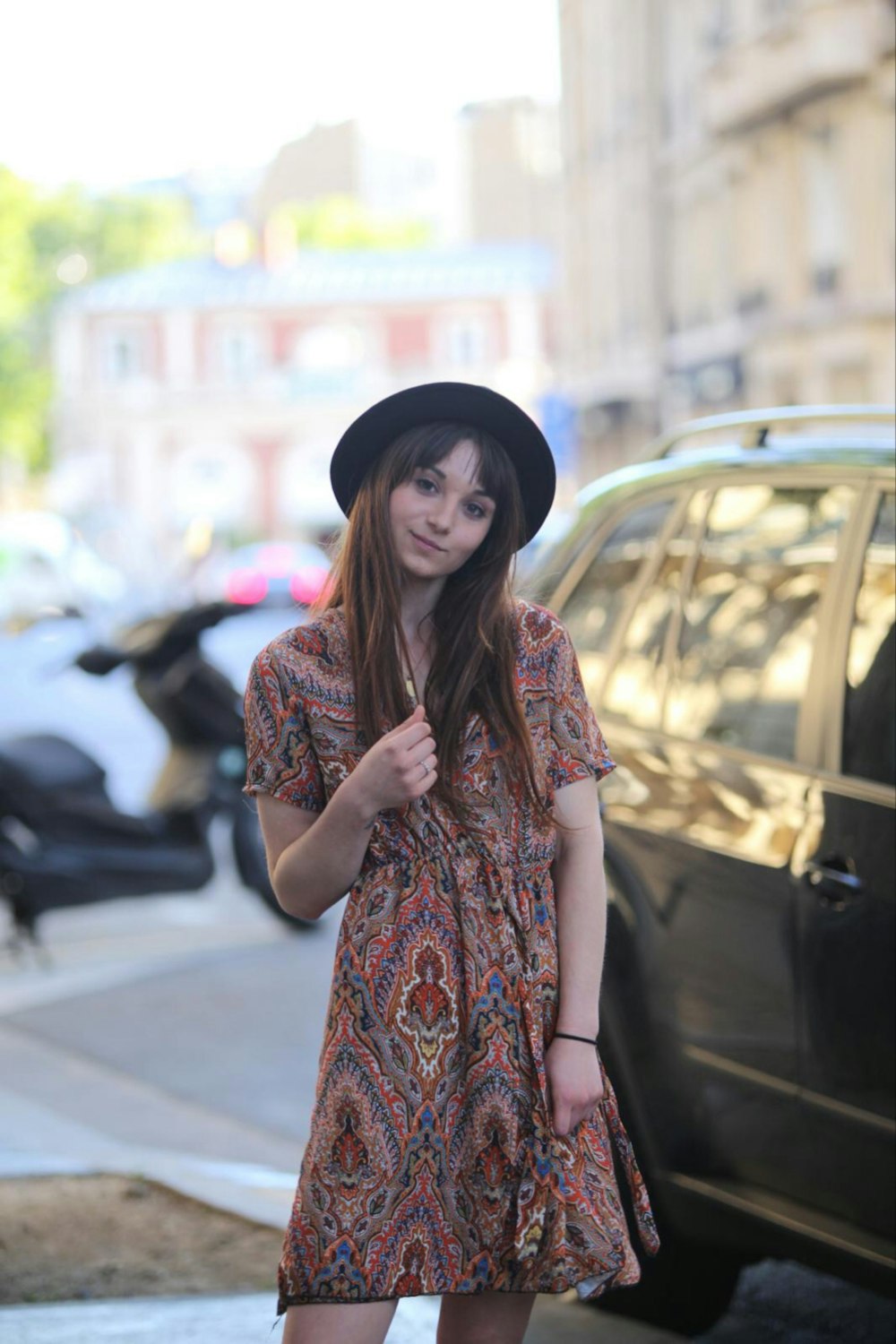 woman in red and brown floral dress wearing black hat standing near black car during daytime