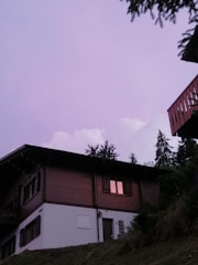 Evening shot of a wooden house with glowing windows and mountain backdrop.