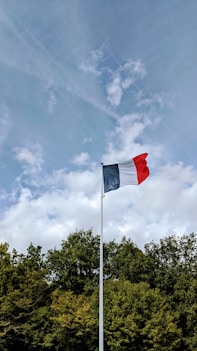 red and white flag on pole under white clouds and blue sky during daytime