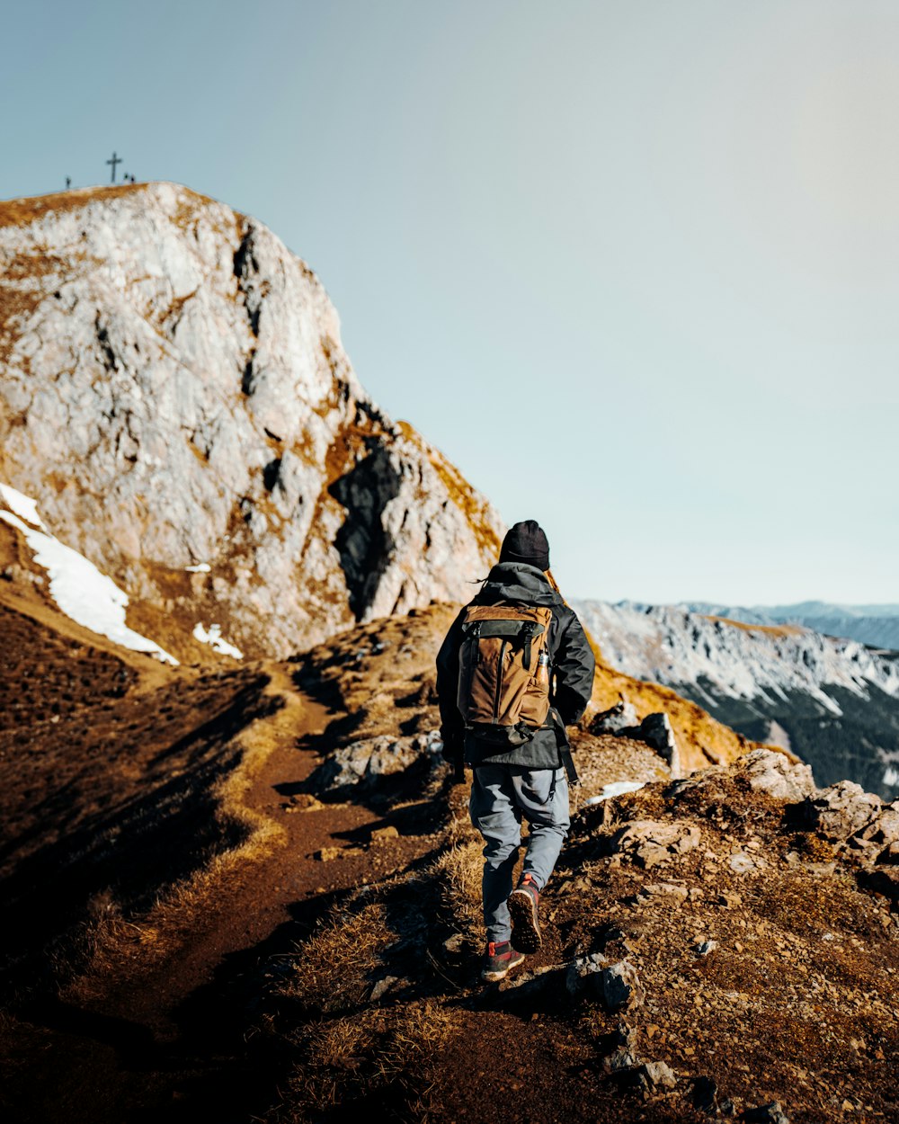 man in brown jacket and gray pants standing on brown rocky mountain during daytime