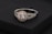 A beautifully crafted ring featuring a large central gemstone surrounded by smaller sparkling stones. The setting is made of intricately designed metal with an elegant blend of silver and gold tones. The ring is displayed on a dark, textured surface.