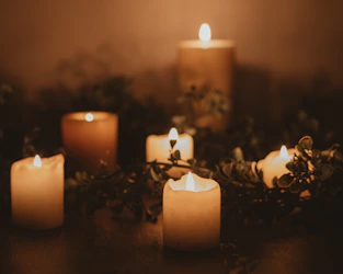 A cozy arrangement of handmade candles glowing softly on a wooden table surrounded by green leaves.