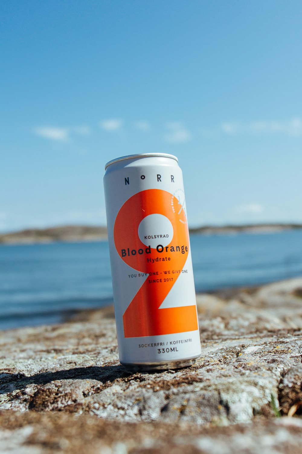 white and orange labeled can on brown sand near sea during daytime