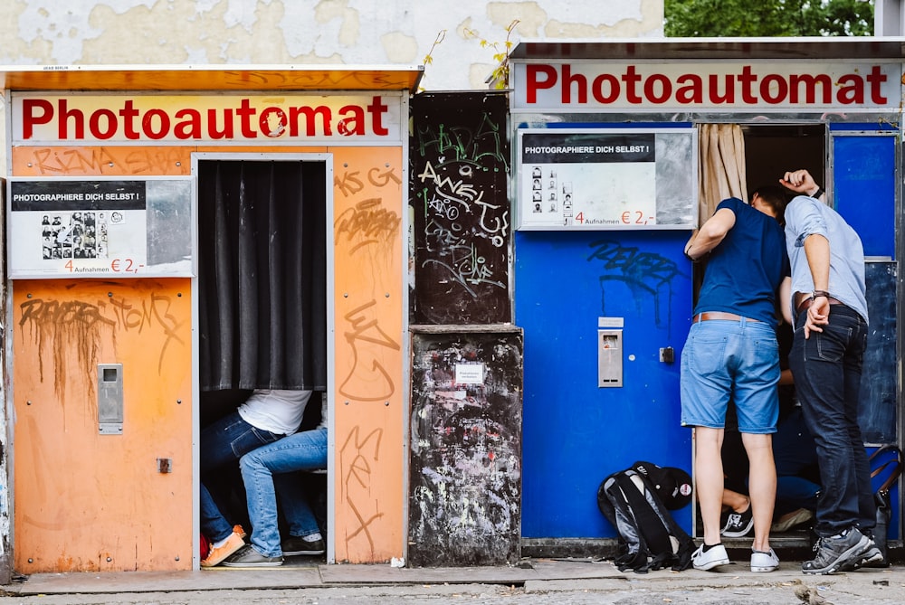 man in blue polo shirt and blue denim jeans standing beside blue and white vending machine