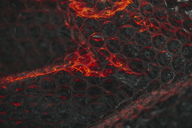 A close-up view of bubble wrap featuring pockets illuminated with red light. The transparent plastic creates a textured and patterned effect with highlights and shadows.