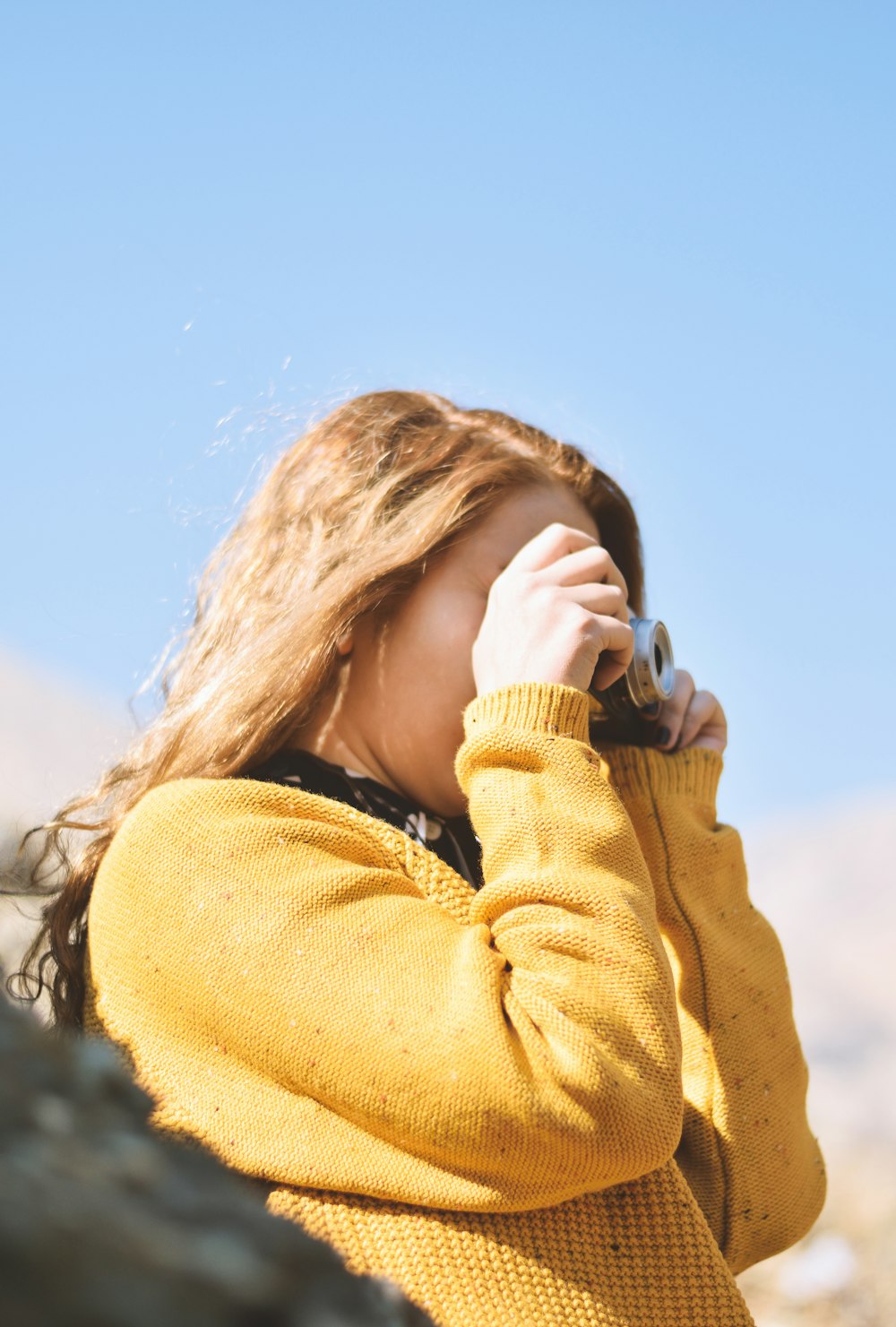 woman in brown sweater holding black and white camera during daytime