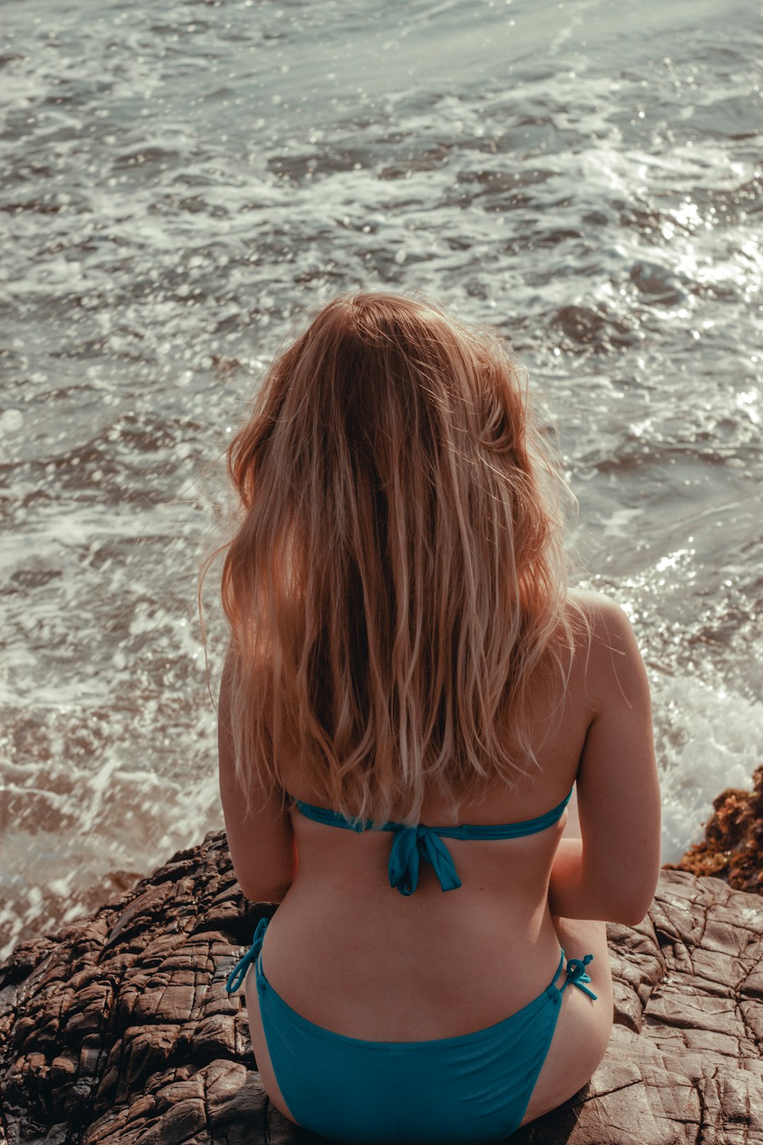 woman in blue bikini top standing on brown rock near sea during daytime