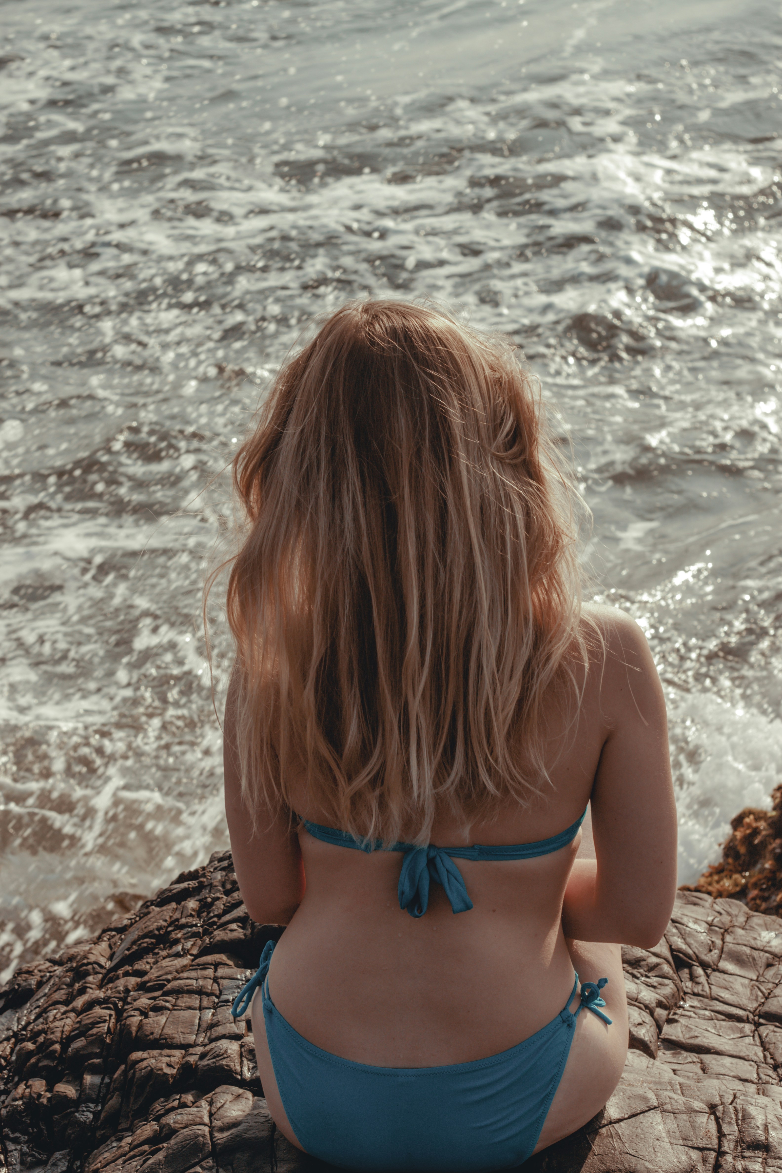woman-in-blue-bikini-top-standing-on-brown-rock-near-sea-during-daytime