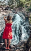 woman in red spaghetti strap dress standing near waterfalls during daytime