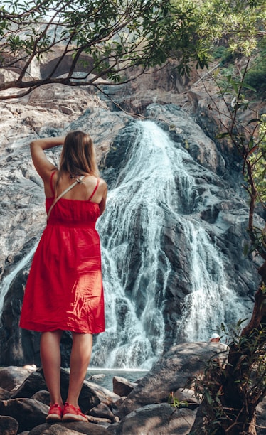 woman in red spaghetti strap dress standing near waterfalls during daytime