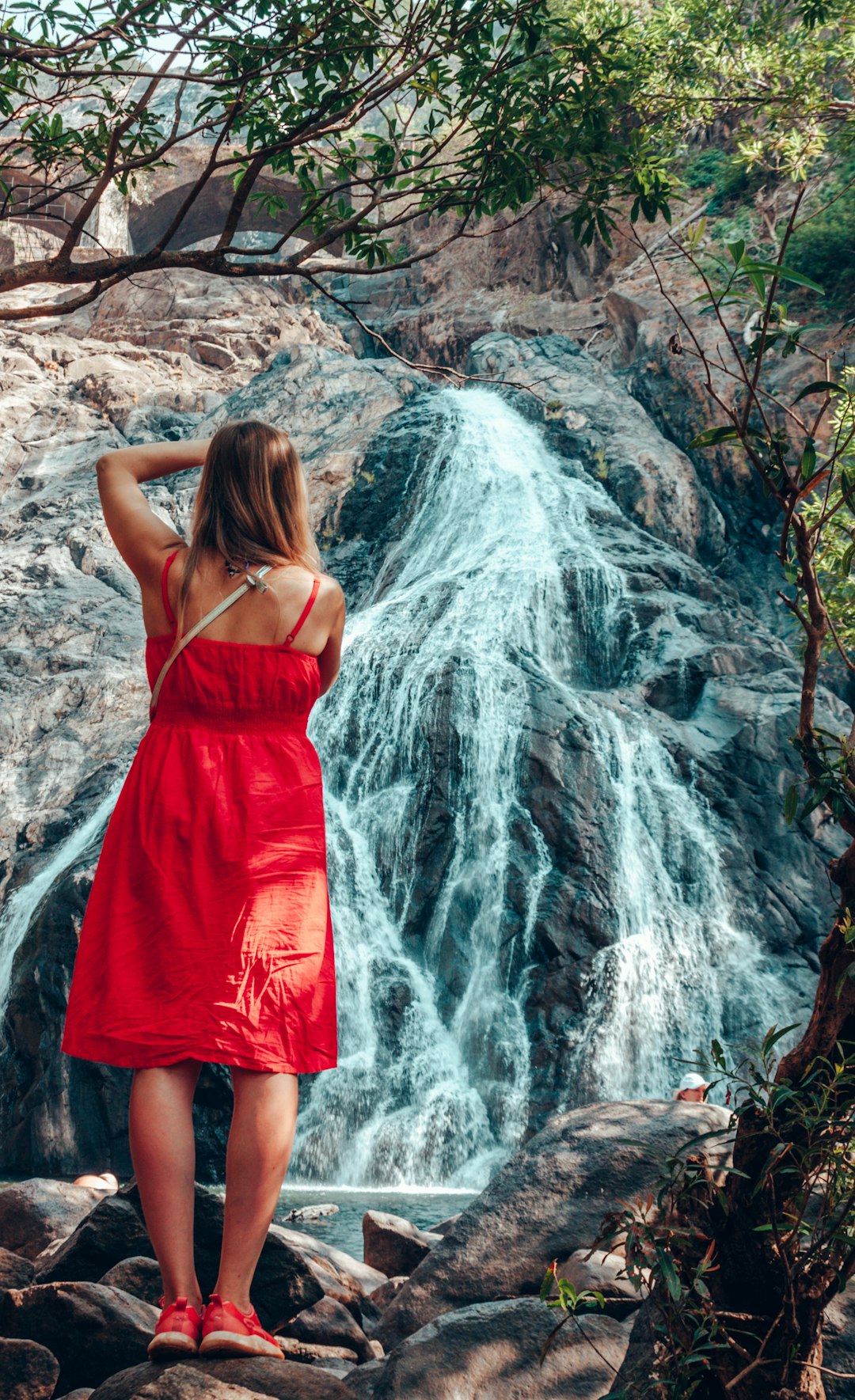woman in red spaghetti strap dress standing near waterfalls during daytime