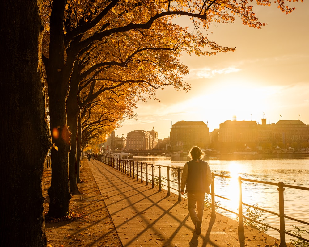 man in black jacket standing on sidewalk near body of water during sunset