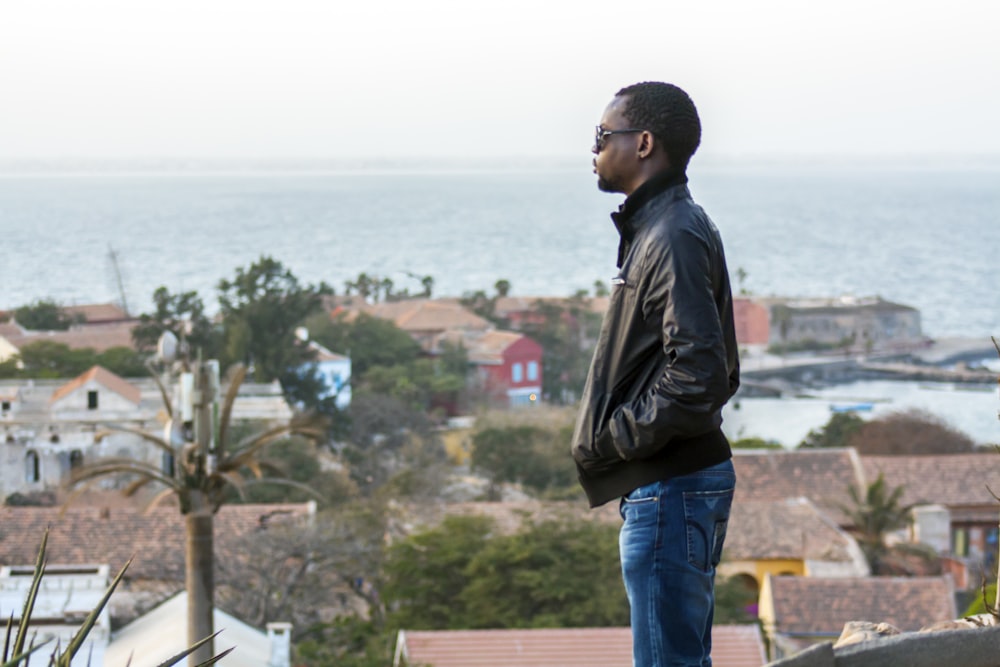 man in black leather jacket standing on top of building looking at the sea during daytime