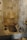 A stone bathroom features a built-in bathtub with antique stone and ceramic vessels placed around its edges. The walls are lined with tiles, and a fabric hangs over a rod on the far wall, adding a rustic and historical atmosphere.