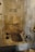 A stone bathroom features a built-in bathtub with antique stone and ceramic vessels placed around its edges. The walls are lined with tiles, and a fabric hangs over a rod on the far wall, adding a rustic and historical atmosphere.