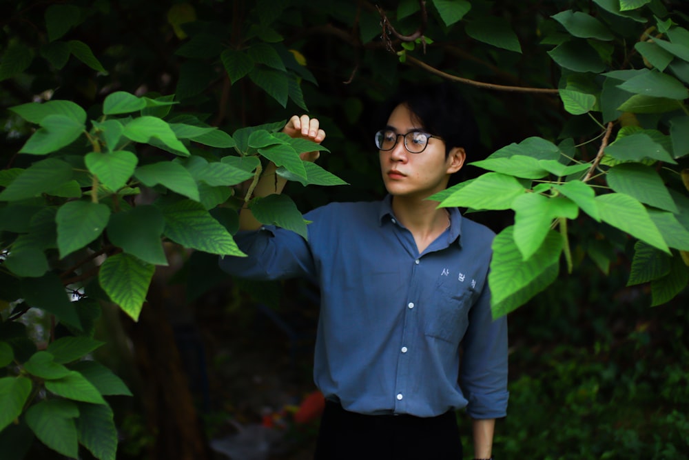 man in blue dress shirt and black pants standing beside green leaves