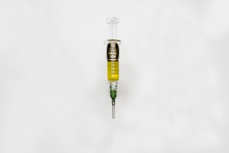 A syringe filled with a golden liquid, labeled 'The Clear Golden Goat', is centered on a white background. The syringe features measurement markings and a green tip.