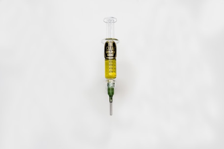 A syringe filled with a golden liquid, labeled 'The Clear Golden Goat', is centered on a white background. The syringe features measurement markings and a green tip.