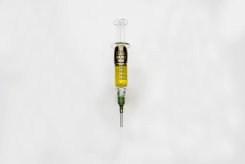 A syringe filled with a golden liquid, labeled 'The Clear Golden Goat', is centered on a white background. The syringe features measurement markings and a green tip.