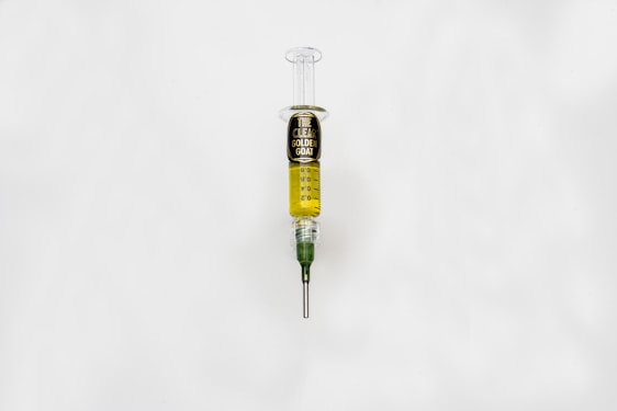 A syringe filled with a golden liquid, labeled 'The Clear Golden Goat', is centered on a white background. The syringe features measurement markings and a green tip.