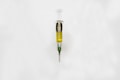 A syringe filled with a golden liquid, labeled 'The Clear Golden Goat', is centered on a white background. The syringe features measurement markings and a green tip.