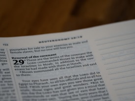 A close-up of a page from a Bible, focusing on Deuteronomy 29, which discusses the renewal of the covenant. The text is printed in a bold, clear font against a light-colored page. The page appears to be in a study or reading environment.