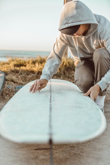 Close-up of hands repairing a surfboard with resin and fiberglass cloth on a sunny beach.