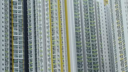 A series of high-rise residential buildings architecturally aligned closely together. The facades display a repetitive pattern of windows and balconies, primarily in white, with accents of yellow and green.