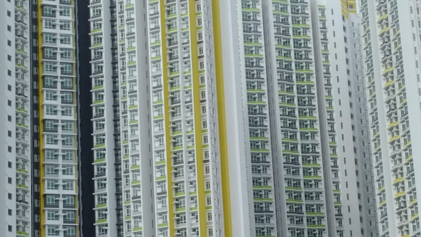 A series of high-rise residential buildings architecturally aligned closely together. The facades display a repetitive pattern of windows and balconies, primarily in white, with accents of yellow and green.