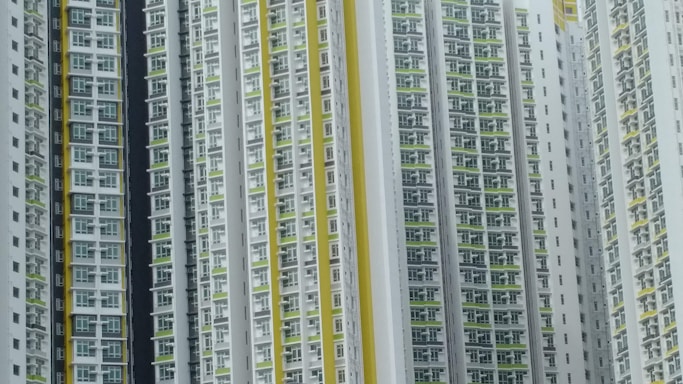 A series of high-rise residential buildings architecturally aligned closely together. The facades display a repetitive pattern of windows and balconies, primarily in white, with accents of yellow and green.