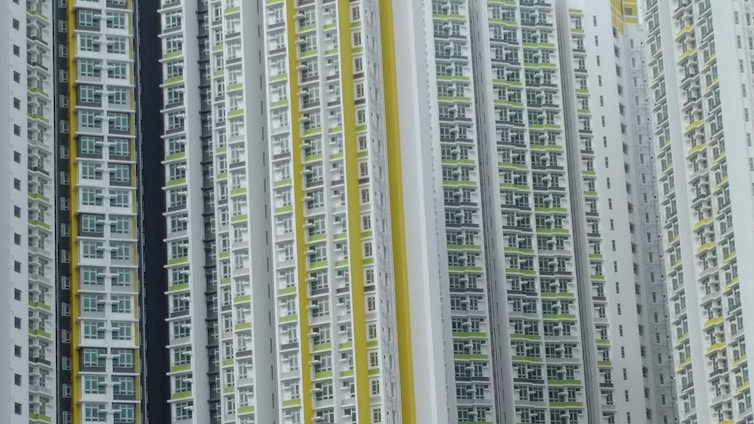A series of high-rise residential buildings architecturally aligned closely together. The facades display a repetitive pattern of windows and balconies, primarily in white, with accents of yellow and green.