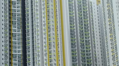 A series of high-rise residential buildings architecturally aligned closely together. The facades display a repetitive pattern of windows and balconies, primarily in white, with accents of yellow and green.