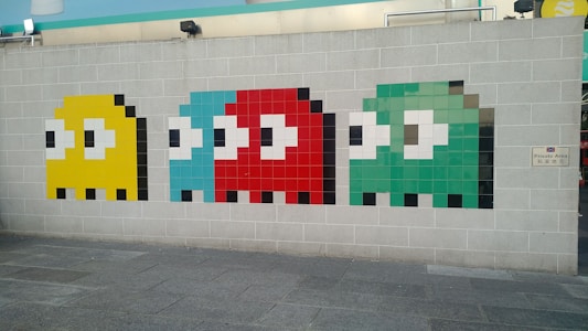 Mosaic art on a grey brick wall depicting four stylized ghost characters in pixelated form. Each ghost is distinct in color: yellow, light blue, red, and green, and they are aligned horizontally. The artwork reflects a retro video game style, reminiscent of classic arcade games. A small sign on the wall reads 'Private Area' in both English and Chinese script.