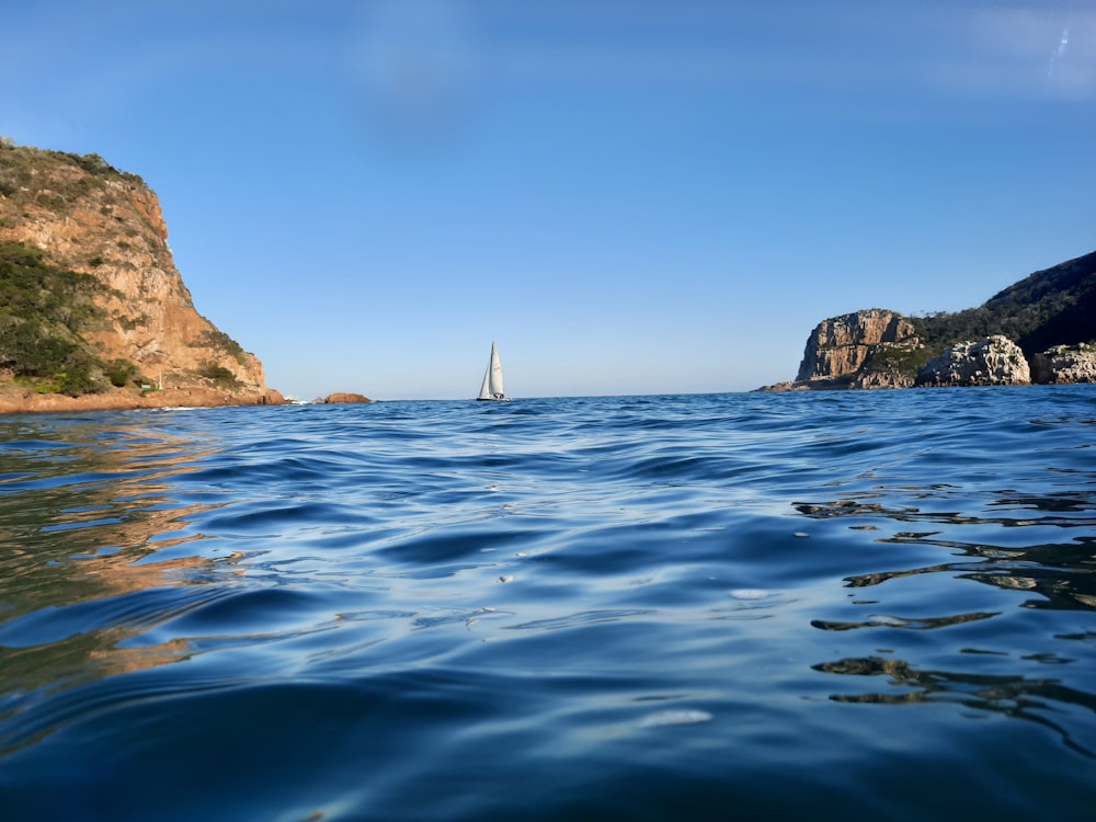 white sailboat on sea near brown rock formation during daytime