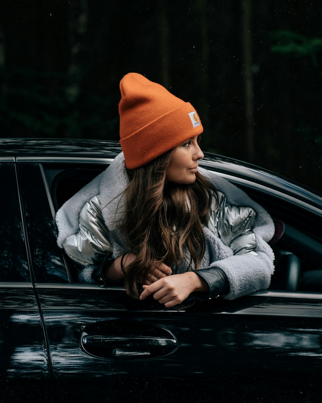 woman in gray jacket and orange knit cap sitting on black car