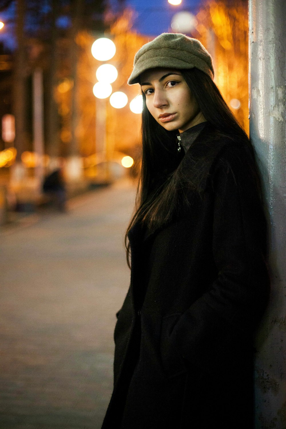 Femme en manteau noir debout près du mur