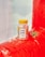 A bottle of CBD gummies labeled 'Not Pot' is placed on a red inflatable surface. The bottle features colorful, playful graphics. Two white bear-shaped gummies and a small green plant are nearby. The soft background includes a subtle view of clouds.