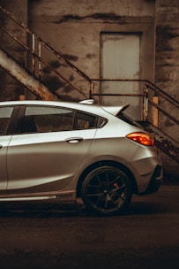 A shiny silver hatchback parked in front of a modern urban building.