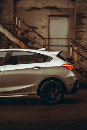 A shiny silver hatchback parked in front of a modern urban building.