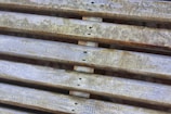 Weathered wooden slats are arranged horizontally, displaying signs of aging with faded paint and patches of moss or dirt. The surface texture is rough and uneven, indicating exposure to the elements over time.
