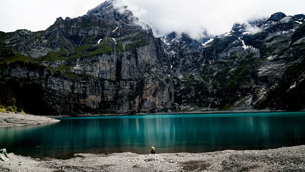 Person im gelben Hemd geht tagsüber auf dem braunen Rocky Mountain in der Nähe von Gewässern spazieren