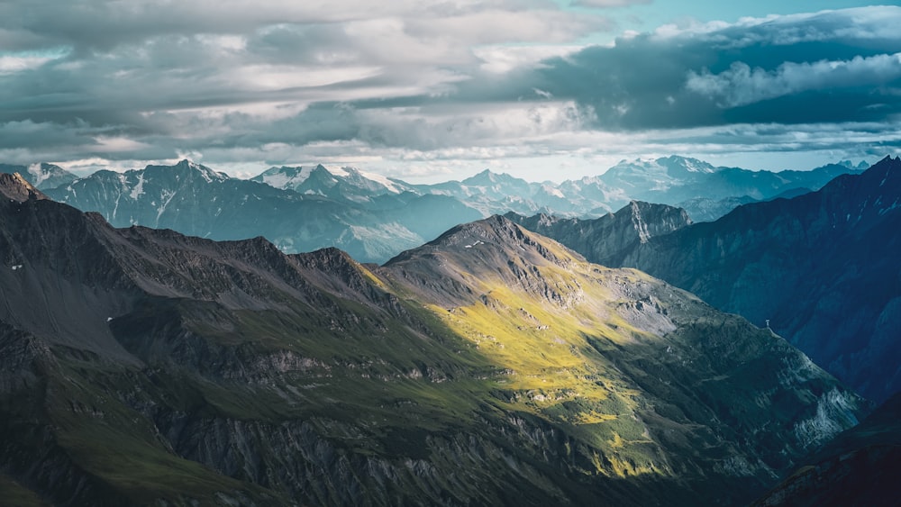 montanhas verdes e marrons sob nuvens brancas e céu azul durante o dia