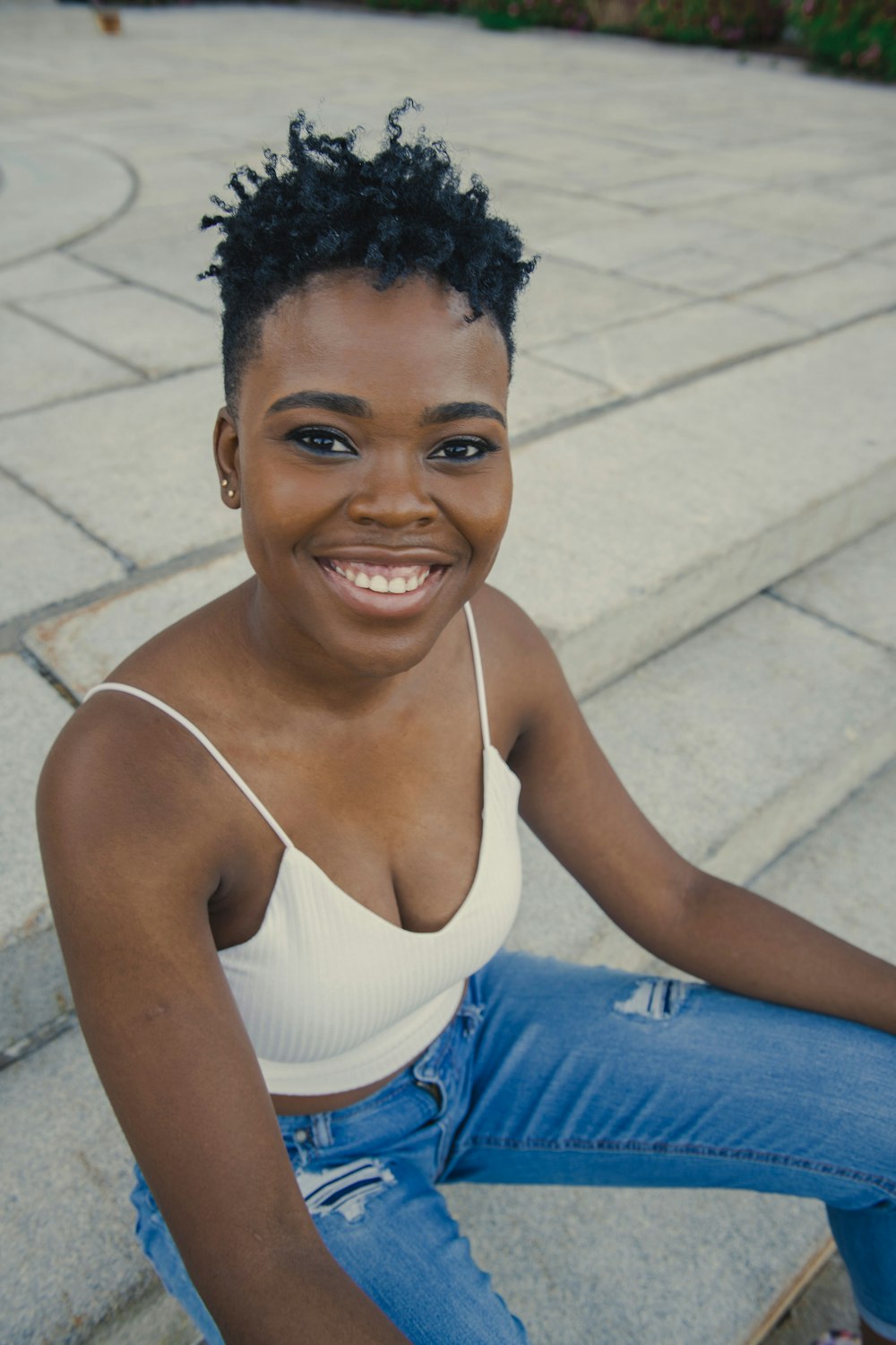 woman in white tank top and blue denim jeans smiling