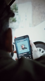 Close-up of a person holding an AudioXM app on a sleek smartphone inside a car.