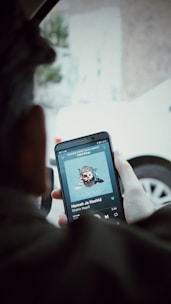 Close-up of a person holding an AudioXM app on a sleek smartphone inside a car.