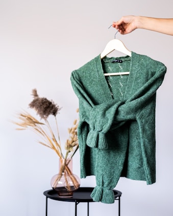 A cozy, hand-stitched pastel green sweater hanging on a wooden hanger.