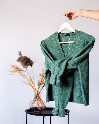 Elegant olive green silk blouse draped on a minimalist hanger against a soft beige background