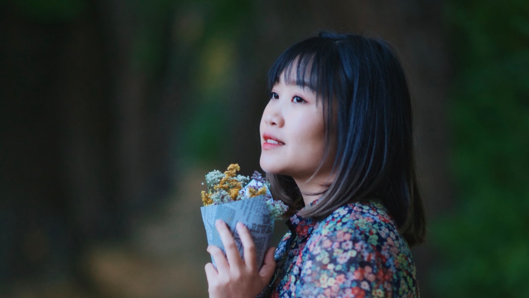 girl in blue and red floral shirt holding white flower